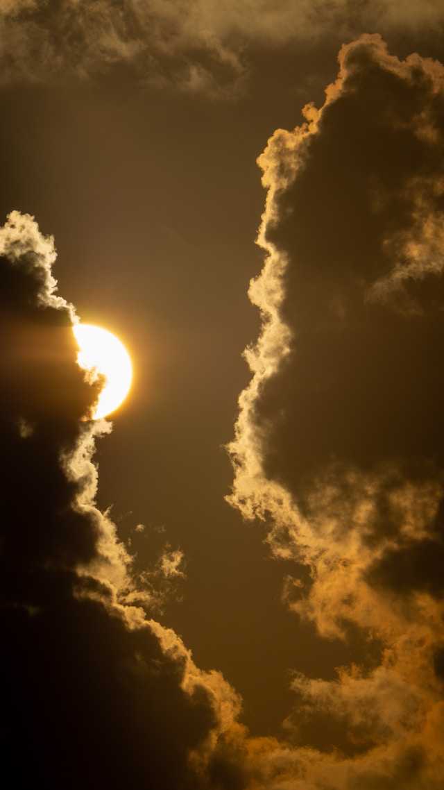 Sun partially obscured by dramatic, dark clouds with golden edges against a warm, glowing sky.