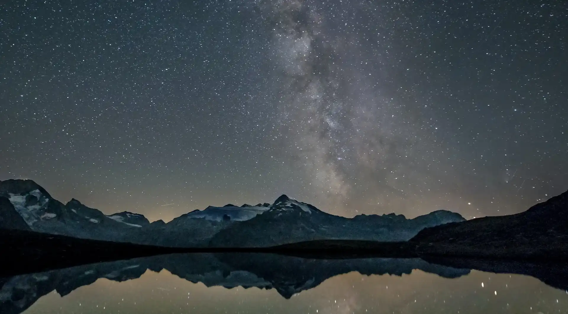 The night sky, reflecting in a lake, surrounded by mountains